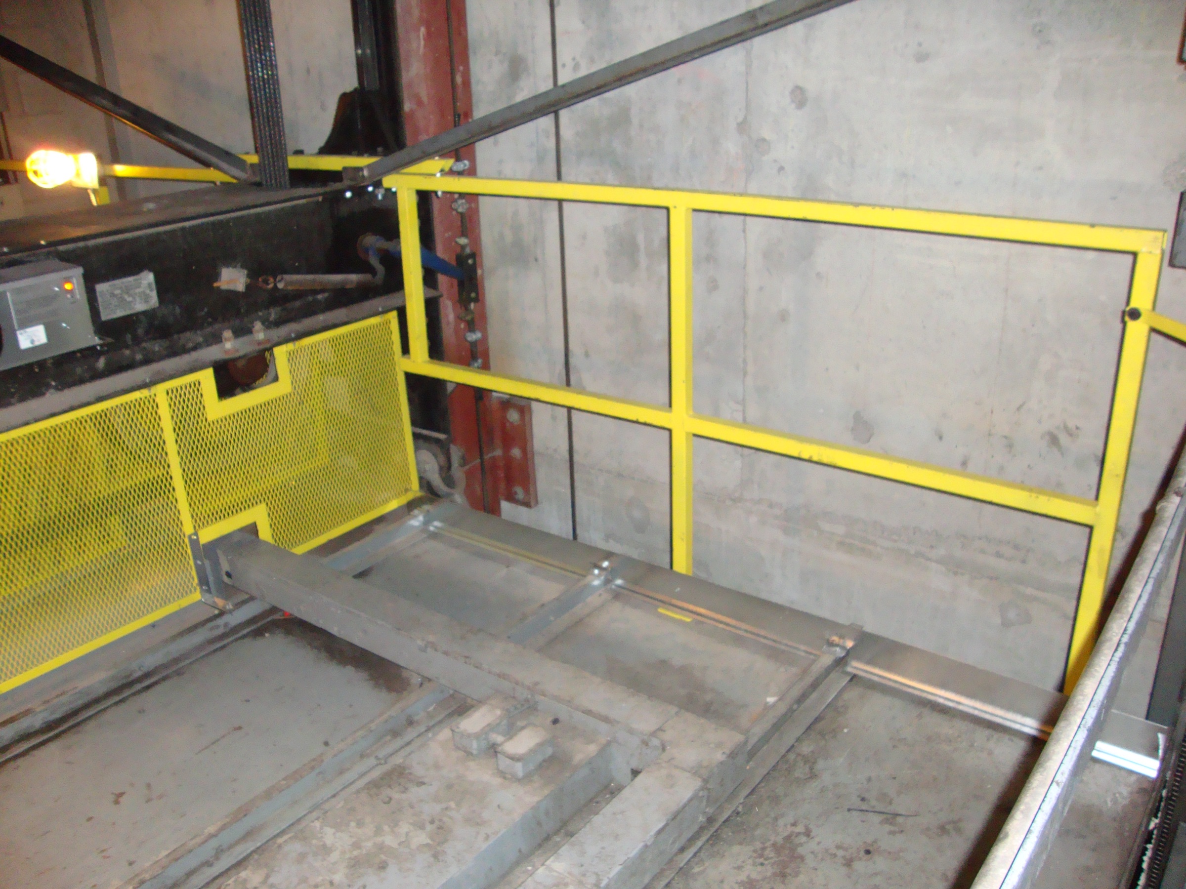 Fixed car top guard rail on a freight elevator car top, with guarding over the car-top sheaves.